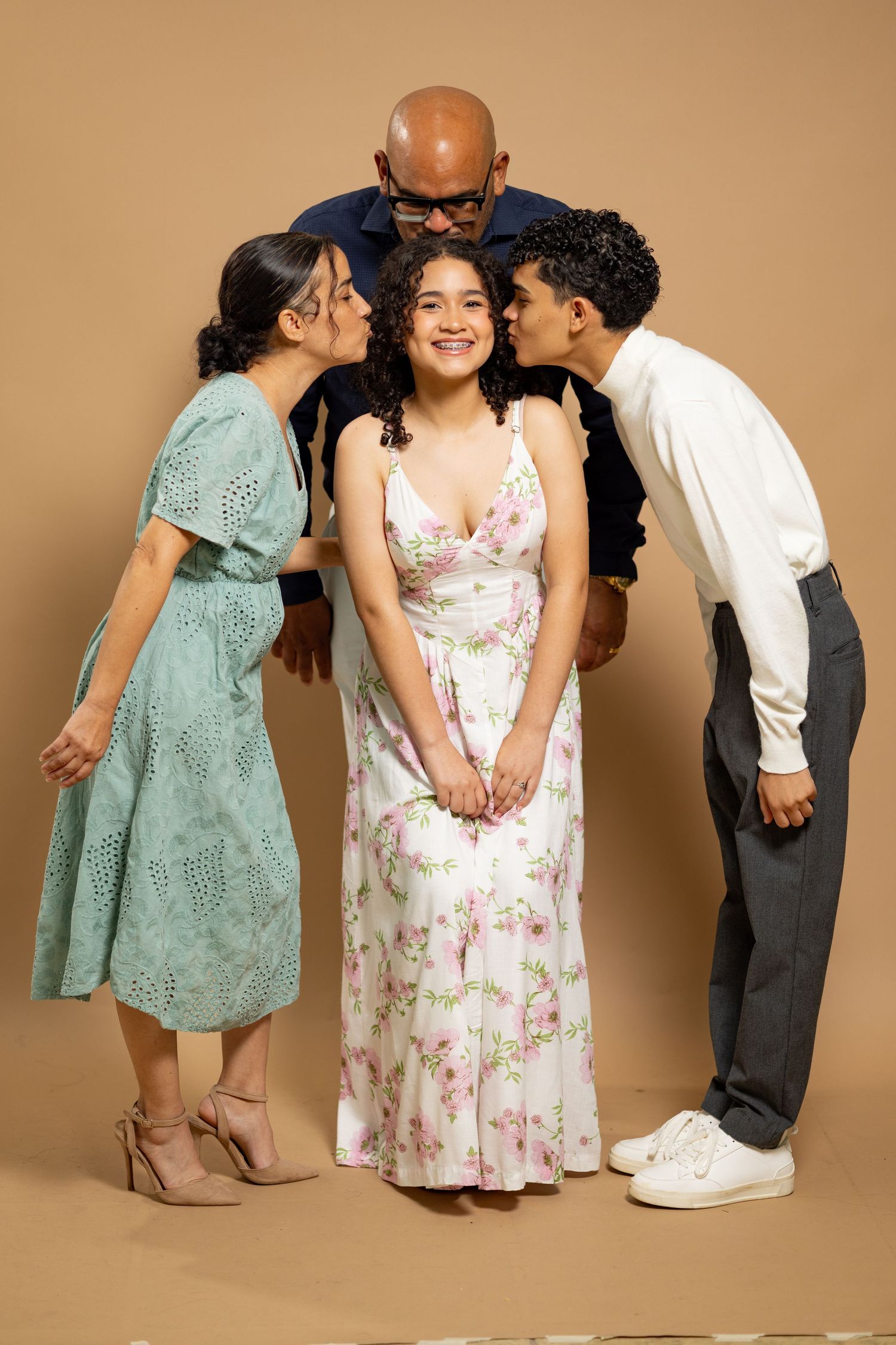 Four people in vintage-style clothing pose playfully against a brown backdrop for a family portrait.
