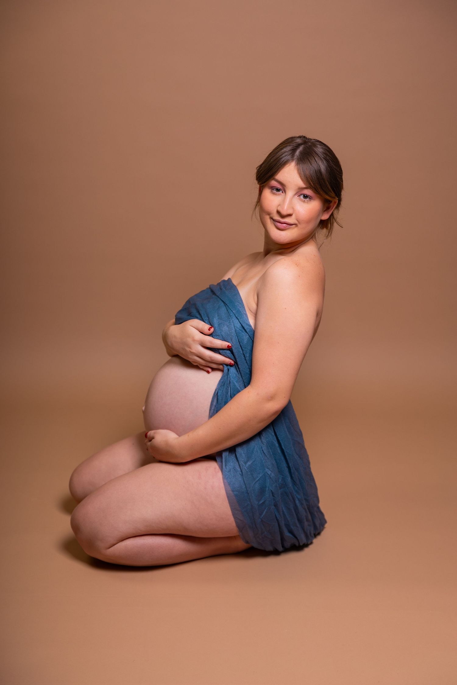 A series of artistic maternity portraits showing a pregnant figure in a blue dress against a warm brown background.