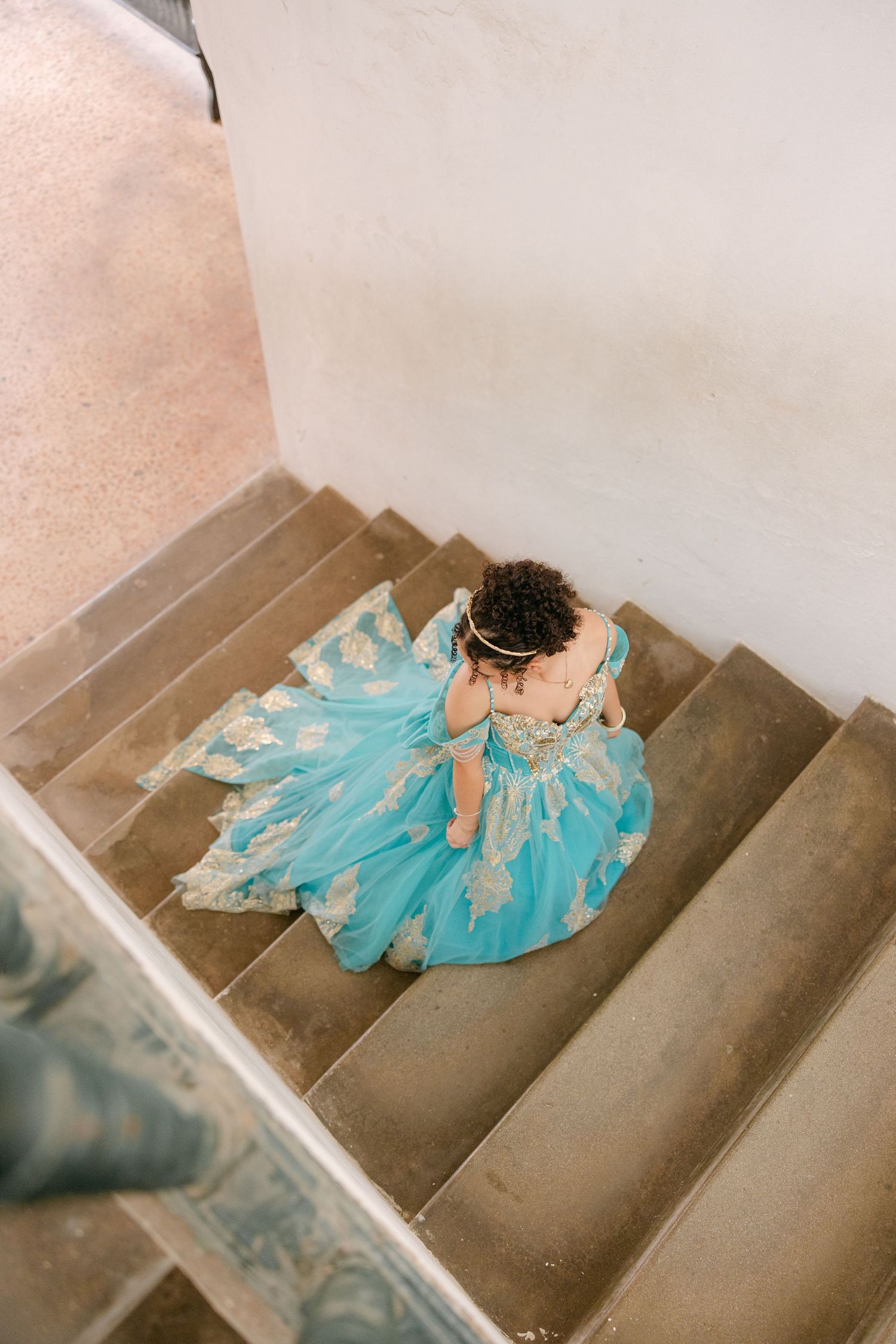 A person in a flowing turquoise dress lies gracefully across concrete stairs in an artistic pose.