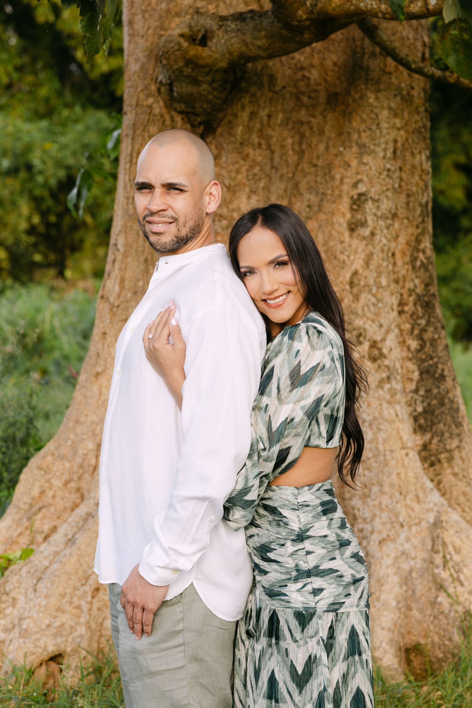 A couple embraces in front of a large tree trunk during an outdoor photo session in a natural setting.