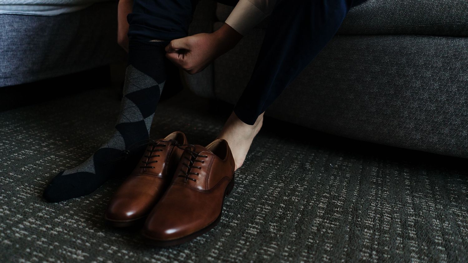Groom putting on brown leather oxford dress shoes on wedding day.