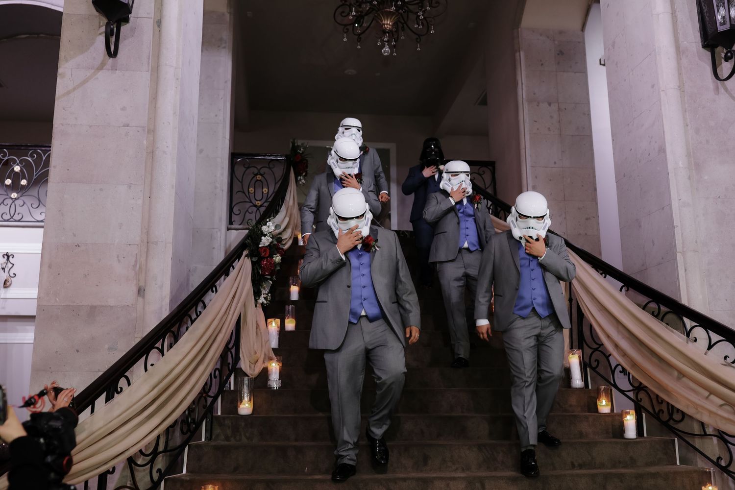Groomsmen wearing Star Wars Stormtrooper helmets descending candlelit staircase.