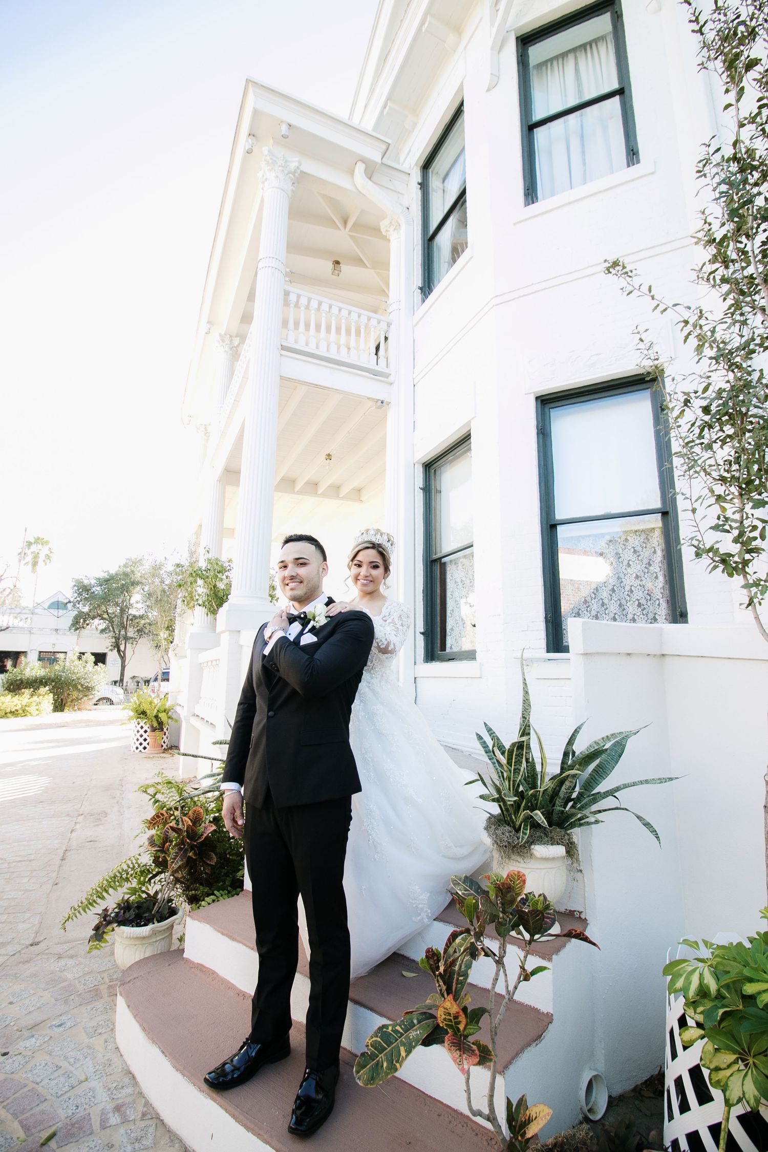 Bride and groom pose together outside a grand white Victorian-style building on their wedding day.