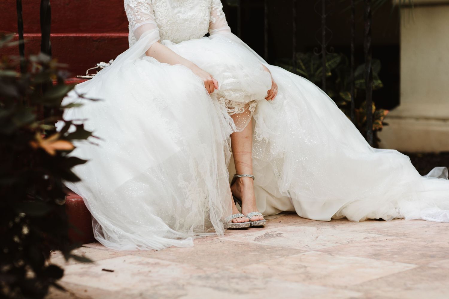 Bride in a white tulle ball gown adjusting her wedding shoes on stone steps.