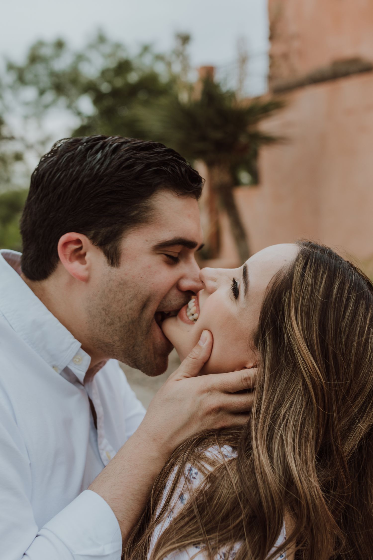 A couple shares a joyful kiss, with the man gently holding the woman's face during an engagement photo session.