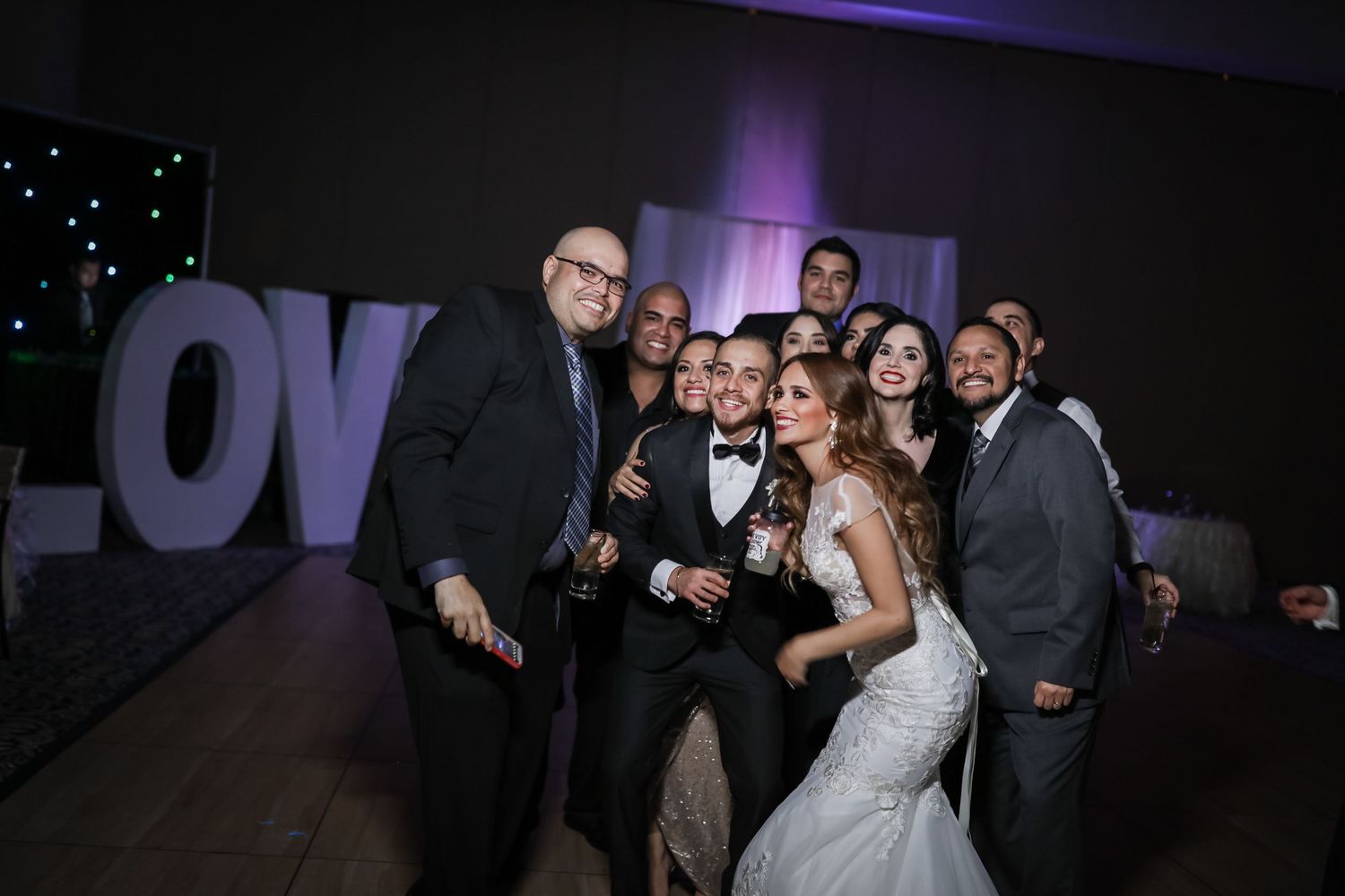 Wedding party group selfie in front of large LOVE letters on dance floor.