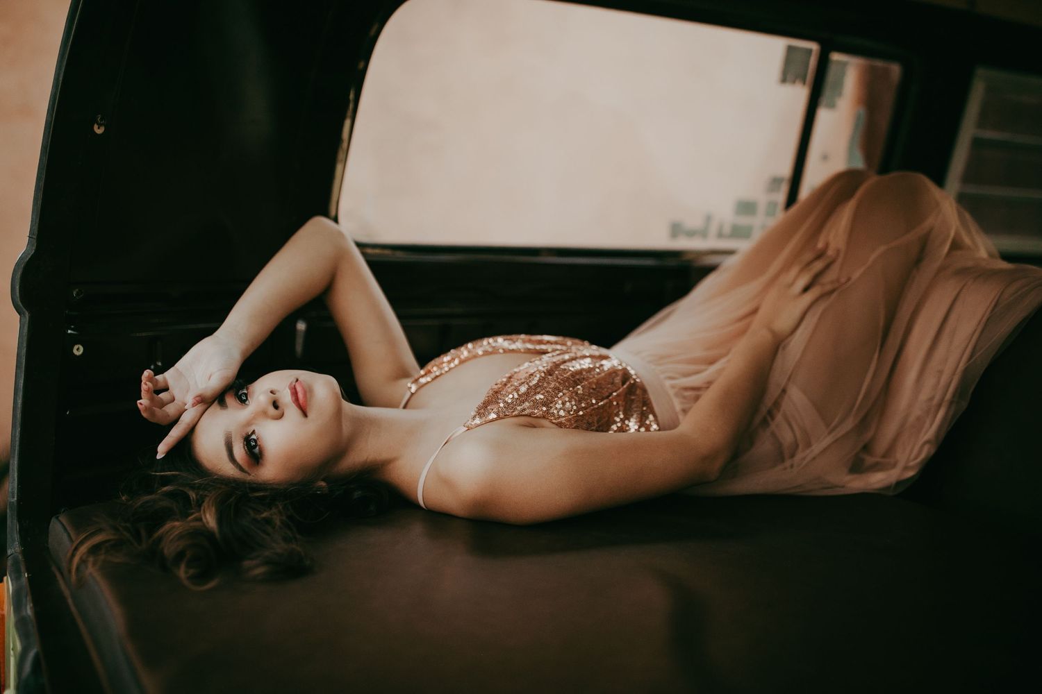 Glamorous boudoir photo featuring a model in a beige lace dress reclining on dark fabric.