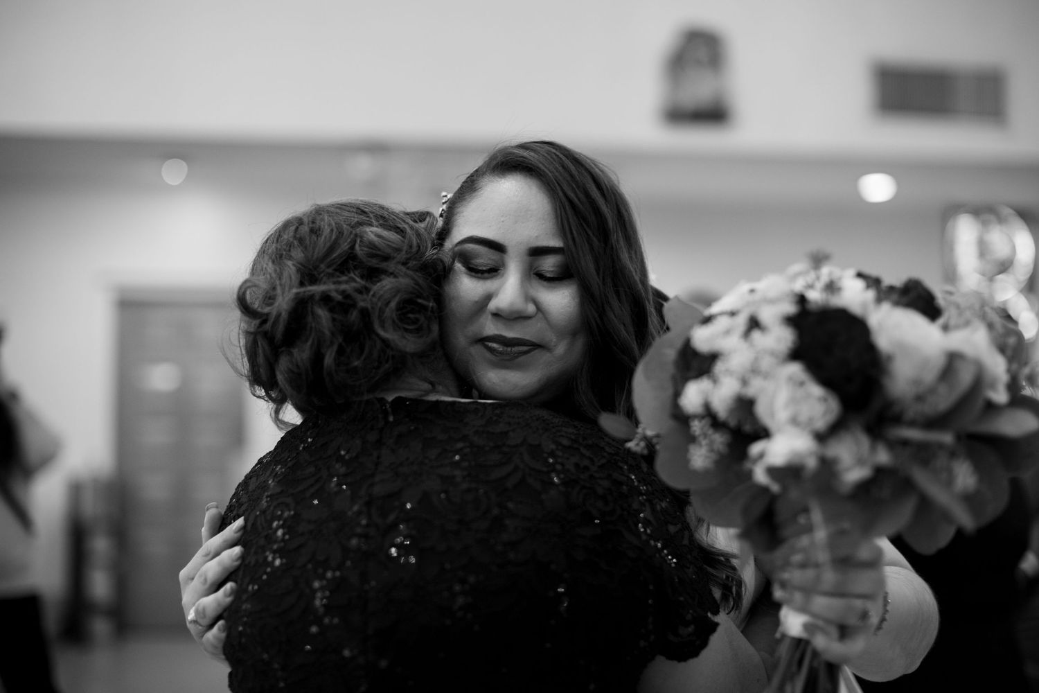 Black and white photo of bride sharing a warm emotional hug with wedding guest.