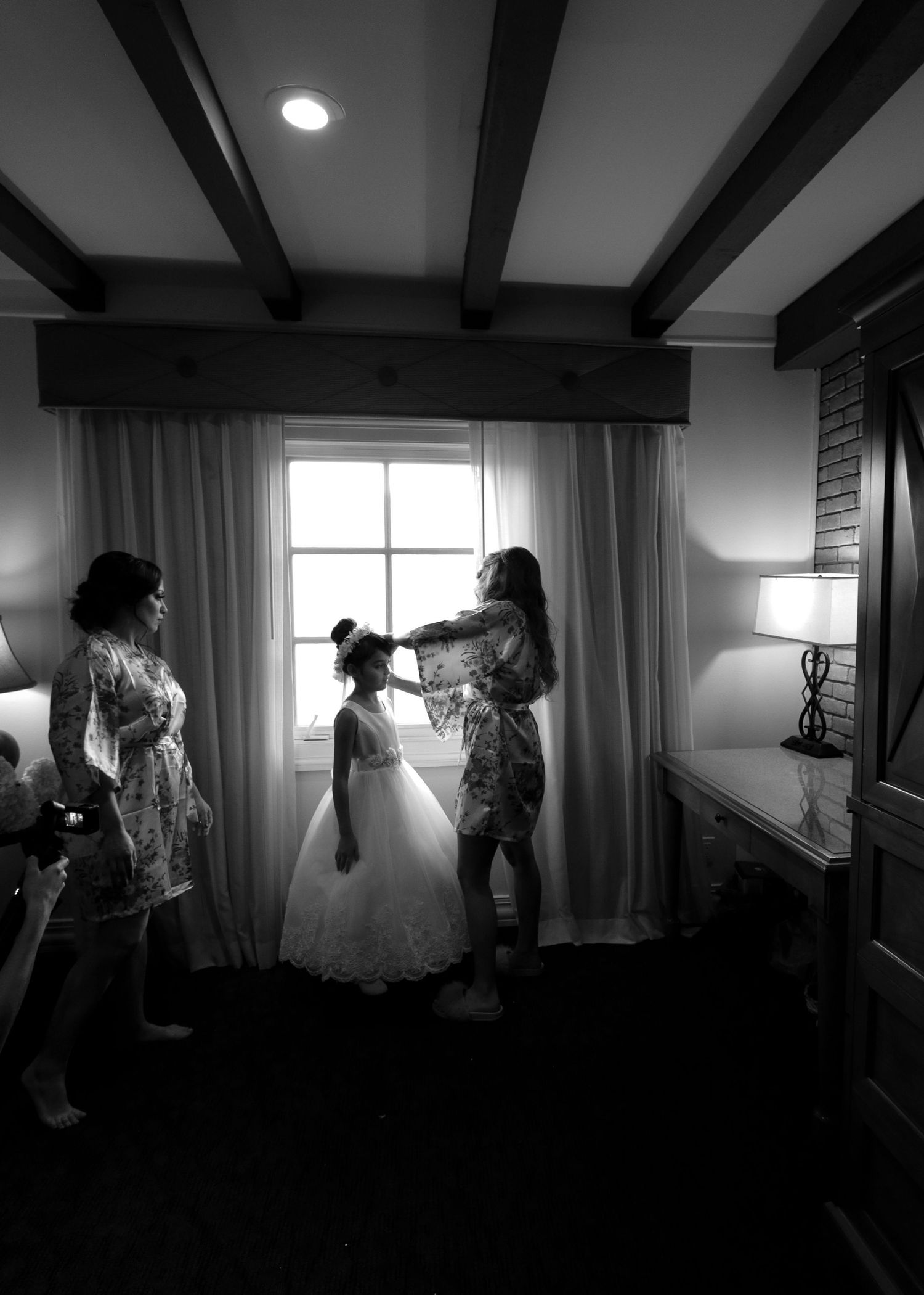 Black and white photo of women helping a flower girl prepare for a wedding in an elegant room.