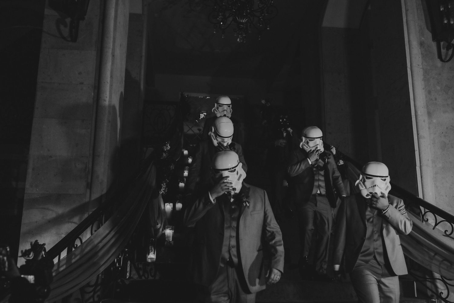 Black and white photo of groomsmen wearing Star Wars stormtrooper helmets on a grand staircase.