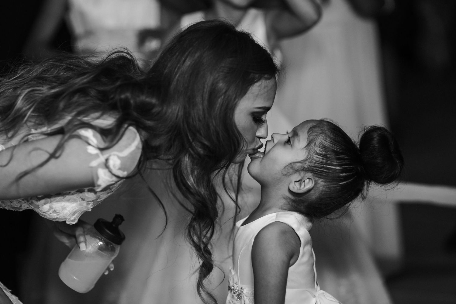 Bride shares a tender kiss with young flower girl in white dress at wedding reception.