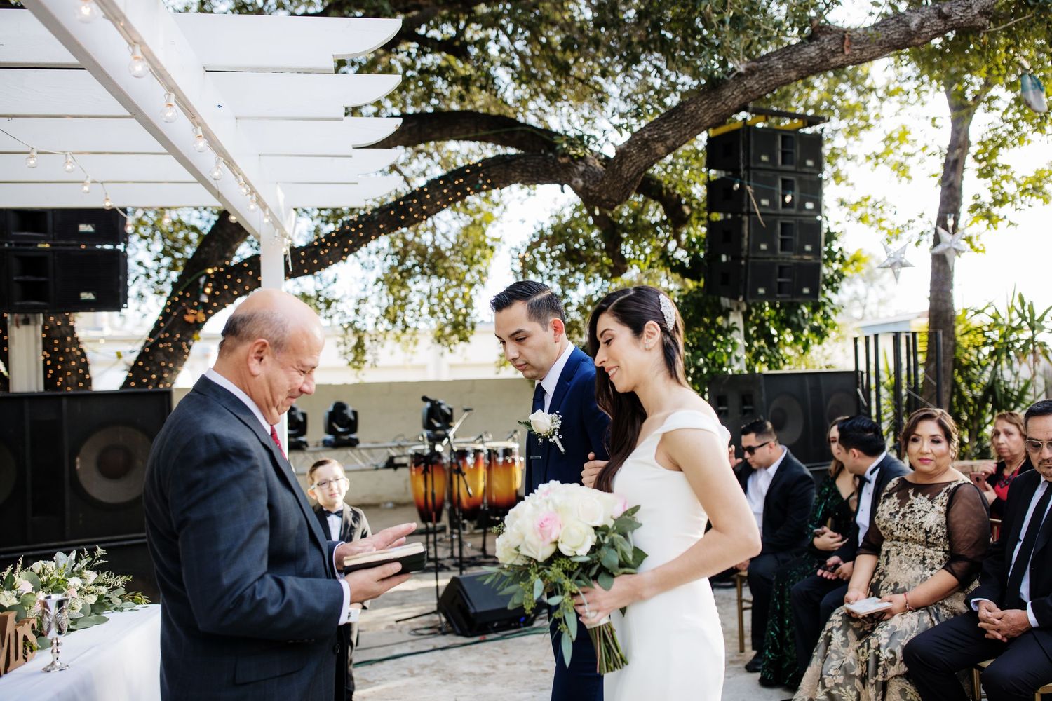 Couple exchanges vows at outdoor wedding ceremony with officiant and white floral decor.