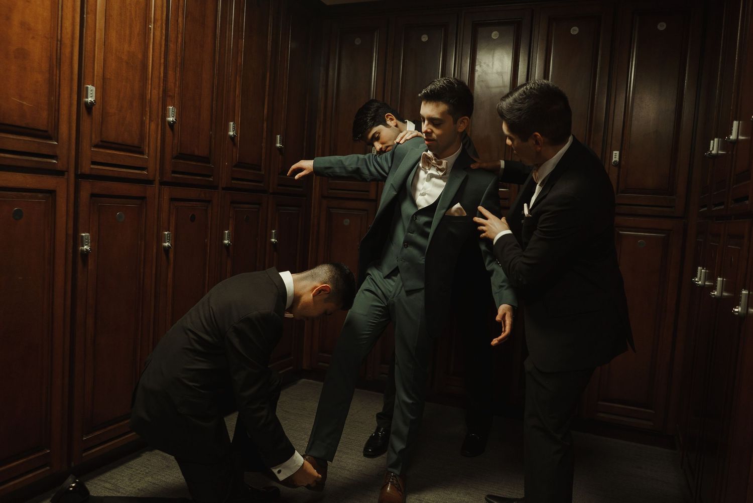 Groomsmen in dark suits share a playful moment together in a wood-paneled locker room before the wedding.