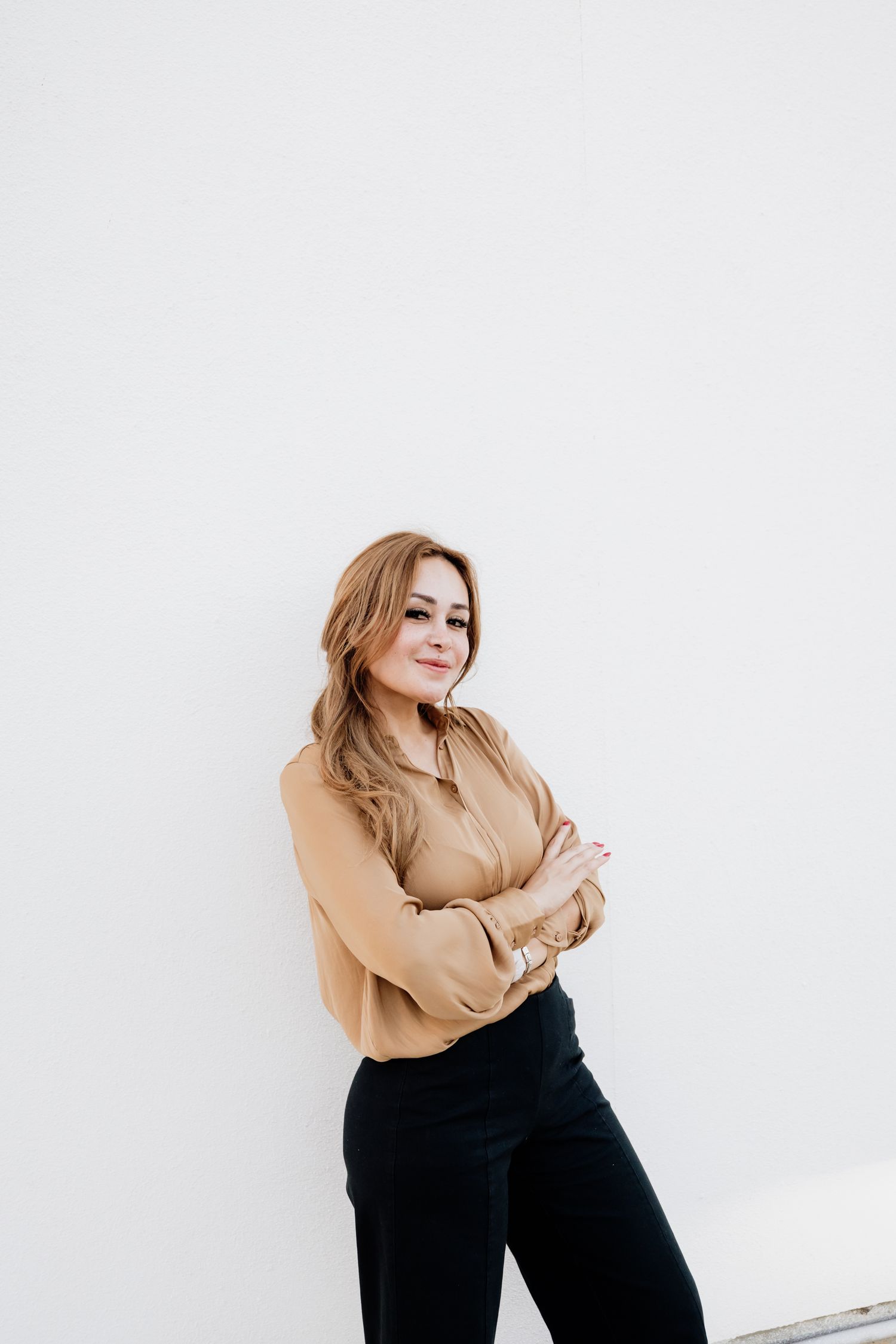 Professional studio portrait of a person posing against white background wearing tan top and black pants.