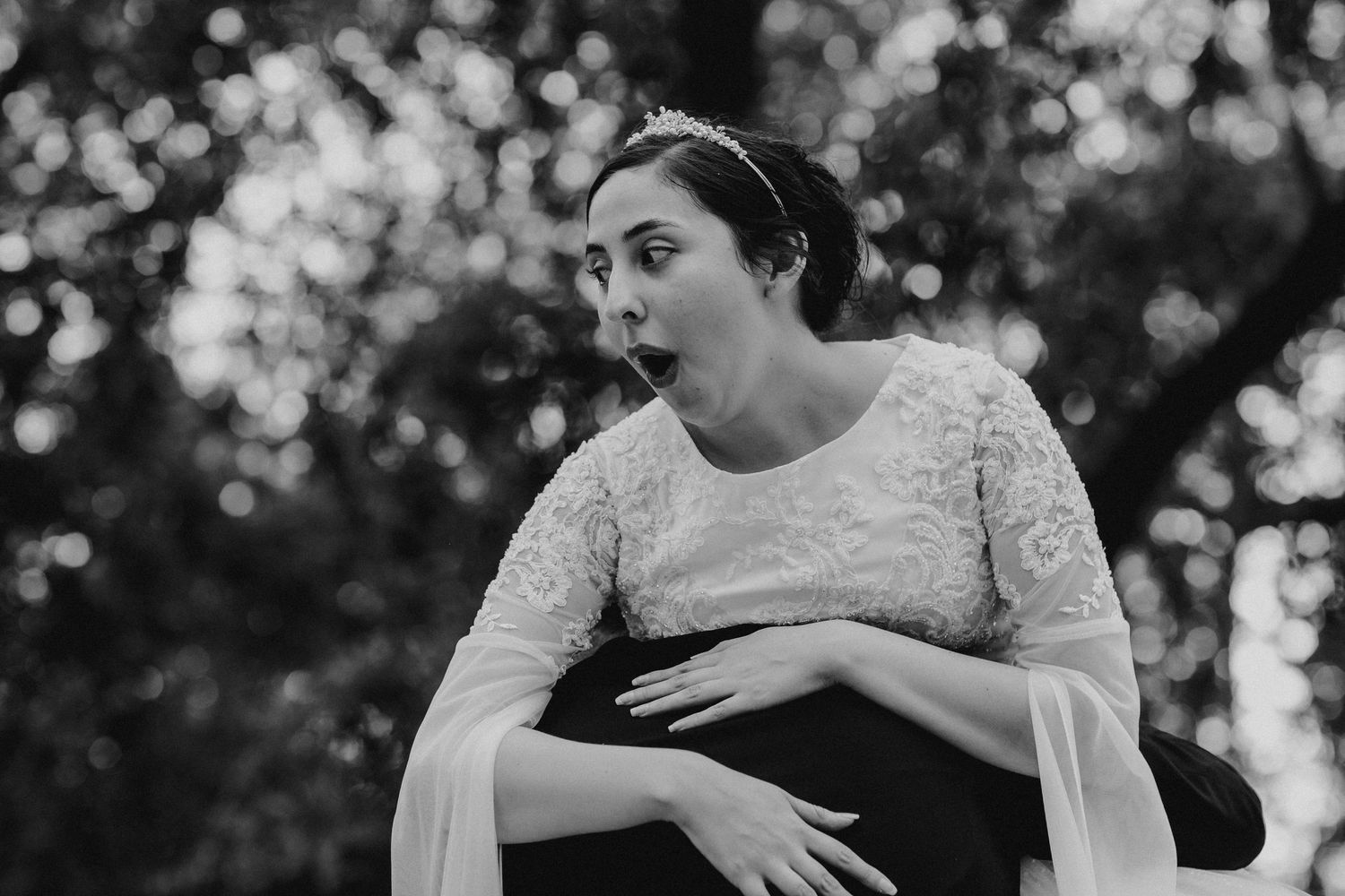 Bride in a lace wedding dress making a surprised expression outdoors in black and white.