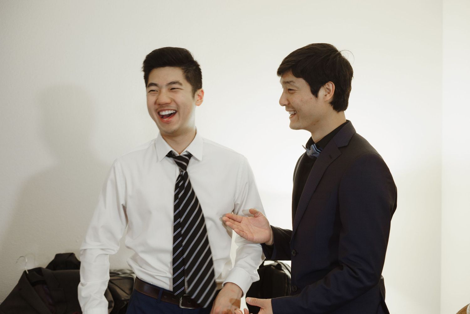 Two men in formal attire laughing together during wedding day preparations.