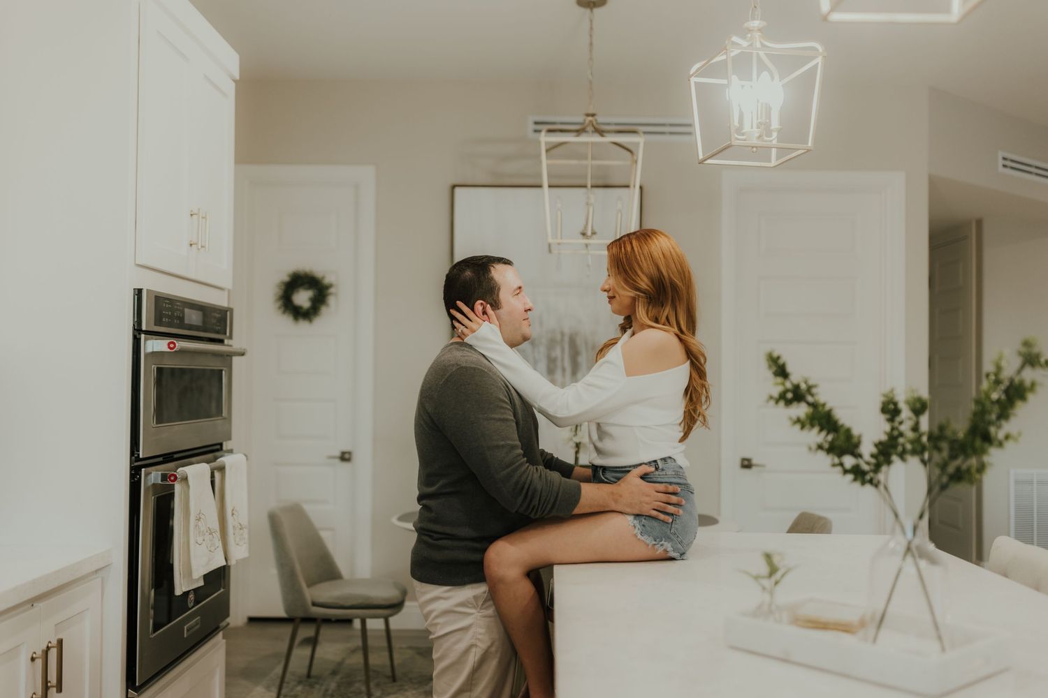 Couple sharing a romantic moment in a bright modern kitchen, woman sitting on counter facing man near island.