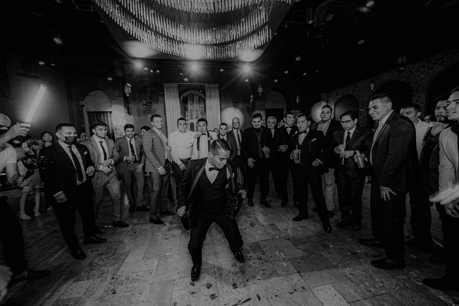Black and white photo of groomsmen dancing in circle at lively wedding reception.