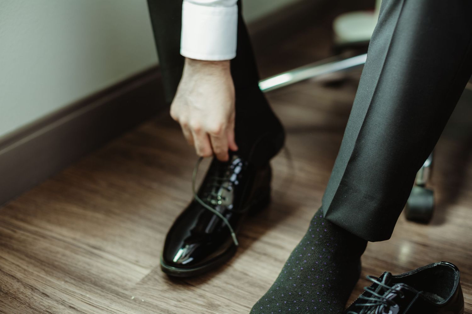 Groom tying black patent leather dress shoes before wedding ceremony.