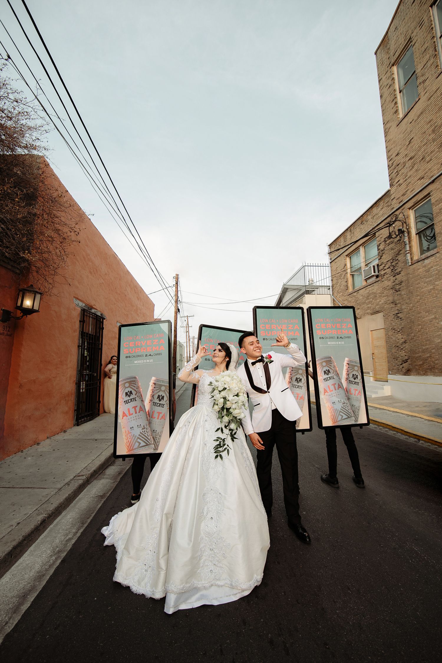 A bride and groom pose in an alley with attendants holding decorative signs on their wedding day.