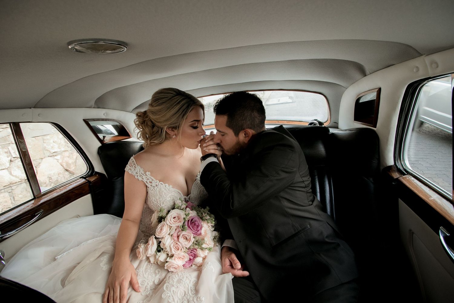 Bride and groom share a romantic moment in the backseat of a vintage wedding car.
