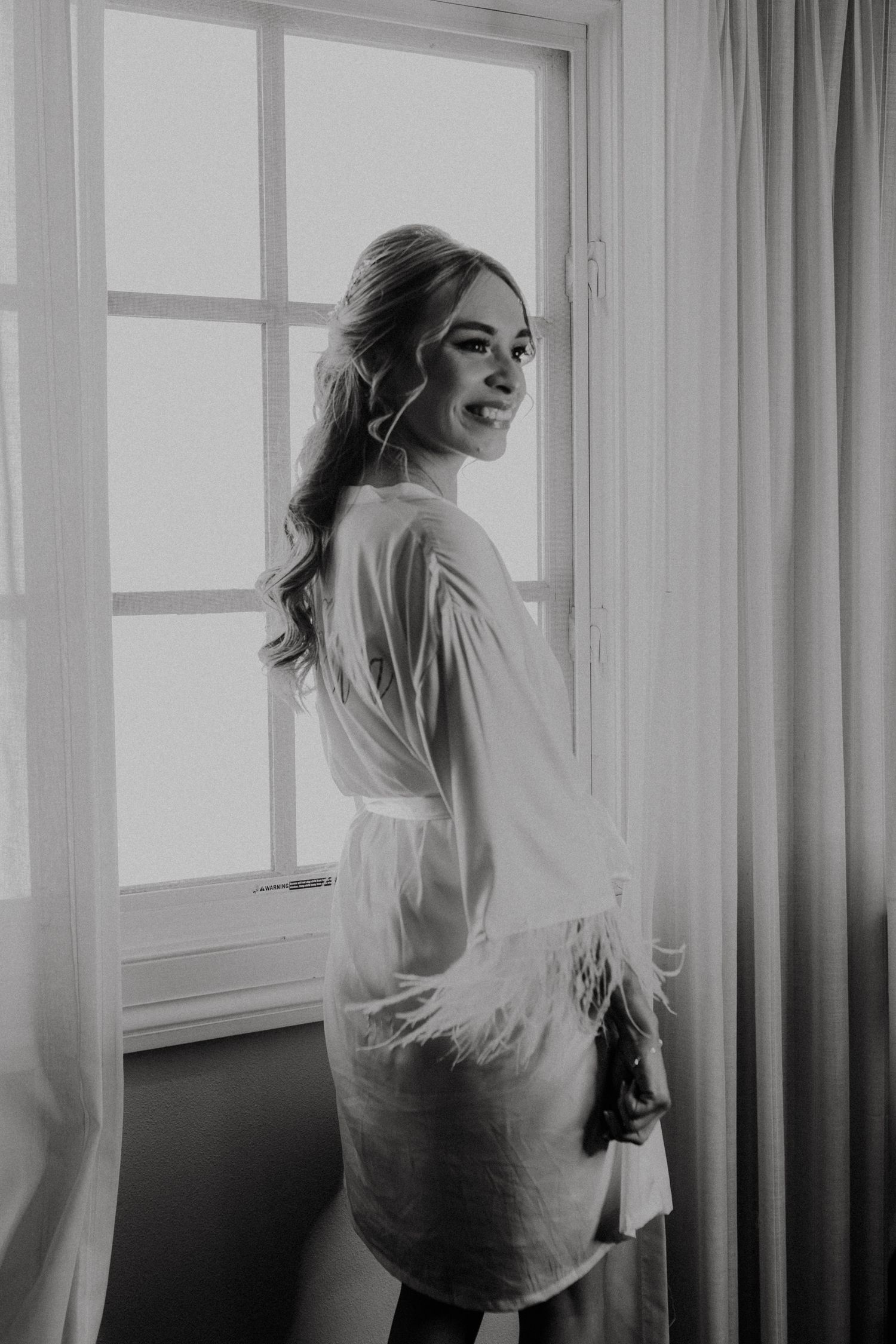 Black and white portrait of a woman in a robe looking back over her shoulder by a window.