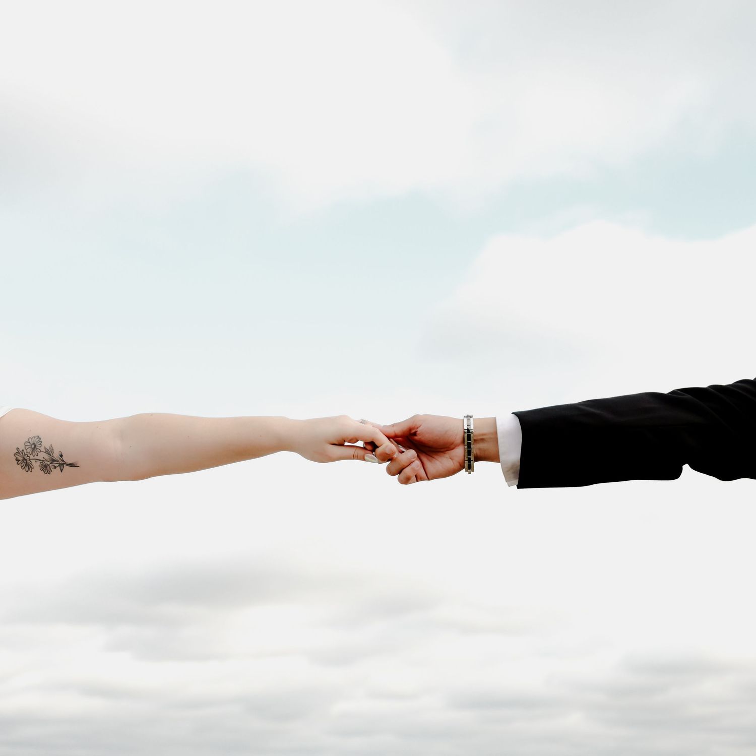 Two hands reach toward each other against a bright sky background, showing a delicate connection.