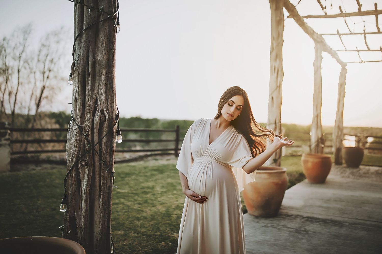 Dreamy maternity photo at sunset under a rustic wooden pergola with desert landscape.