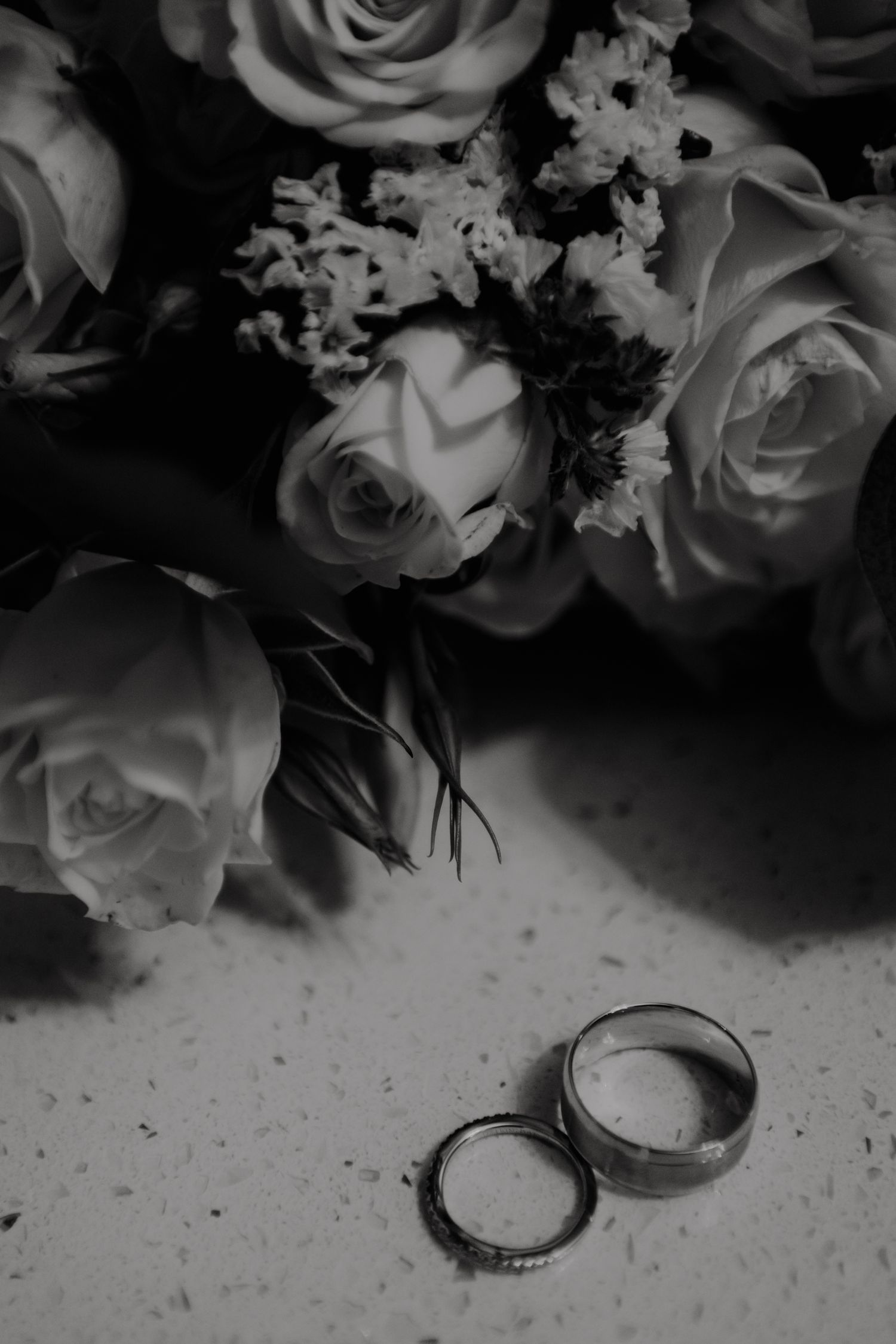 Artistic black and white photo of wedding rings with roses and floral arrangements.