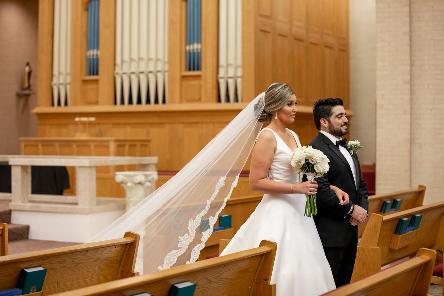 Bride in lace veil and groom walking down the aisle of a church after their wedding ceremony.