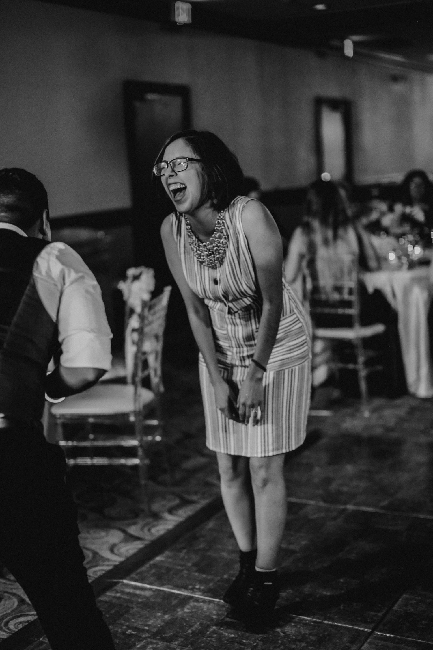 Woman laughing joyfully while dancing at a wedding reception in a striped dress.