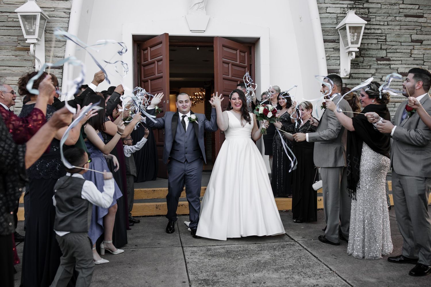 A bride and groom exit a church as guests celebrate with streamers and ribbons.