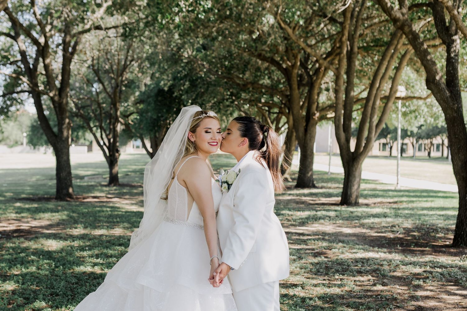 Wedding couple shares a romantic moment under sunlit trees in a garden setting.
