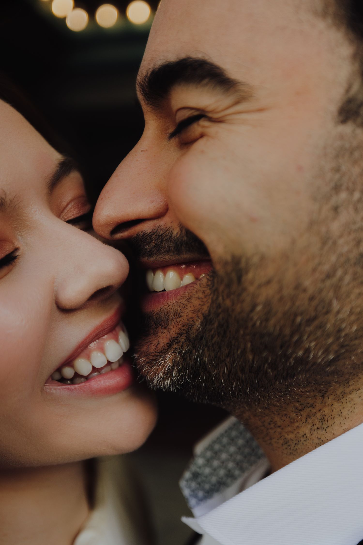 Close-up of a smiling couple cheek to cheek, man with beard whispering to woman, romantic intimate moment.