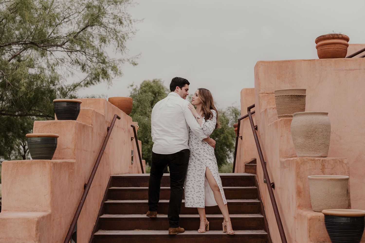 Couple sharing a romantic moment on adobe steps surrounded by terracotta pots and lush greenery.