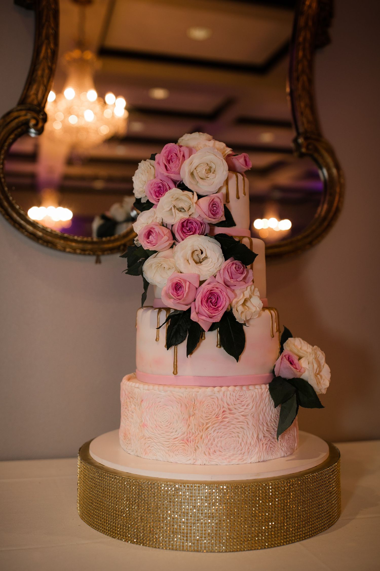 Elegant three-tier pink wedding cake adorned with pink and white roses on a gold sequin stand.