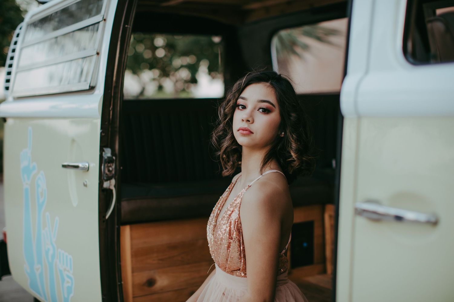 A woman in an elegant peach dress poses on wooden stairs in soft natural lighting.
