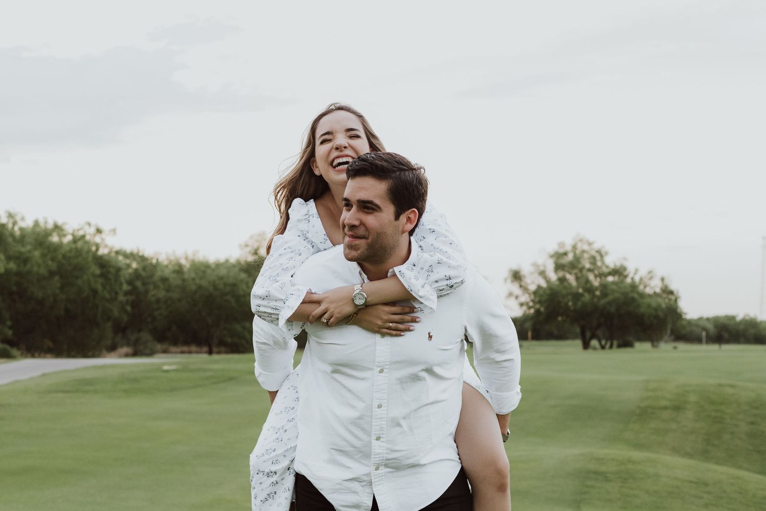 A happy couple in white shirts, woman piggyback riding on mans back outdoors.