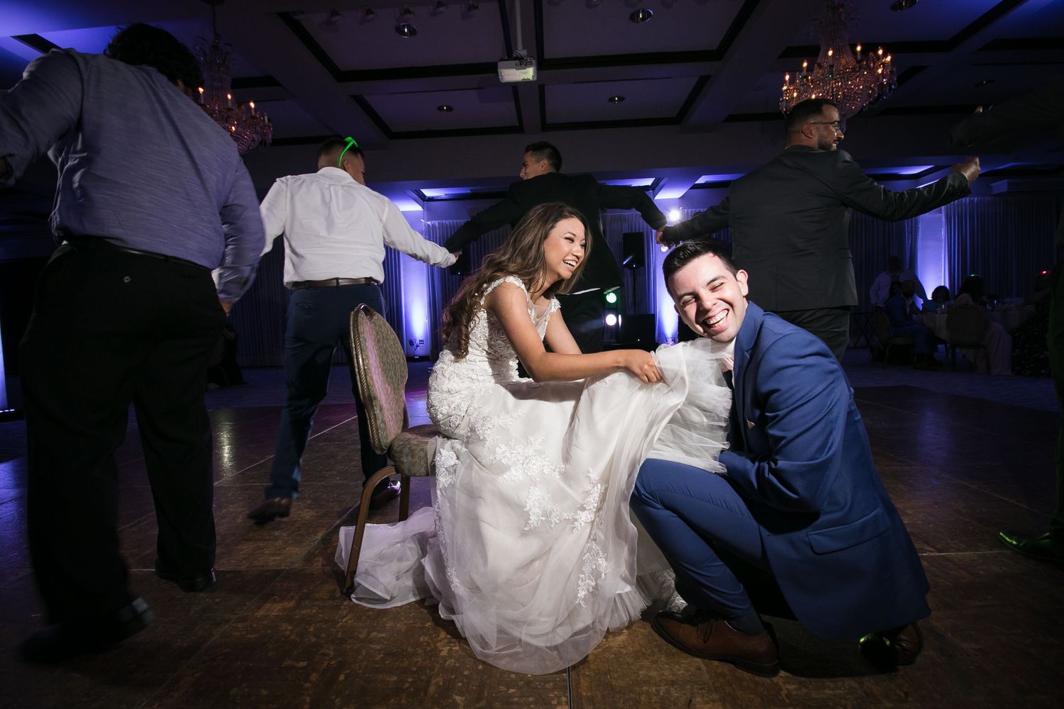Bride and groom share a joyful dance floor moment, laughing together during wedding reception celebration.