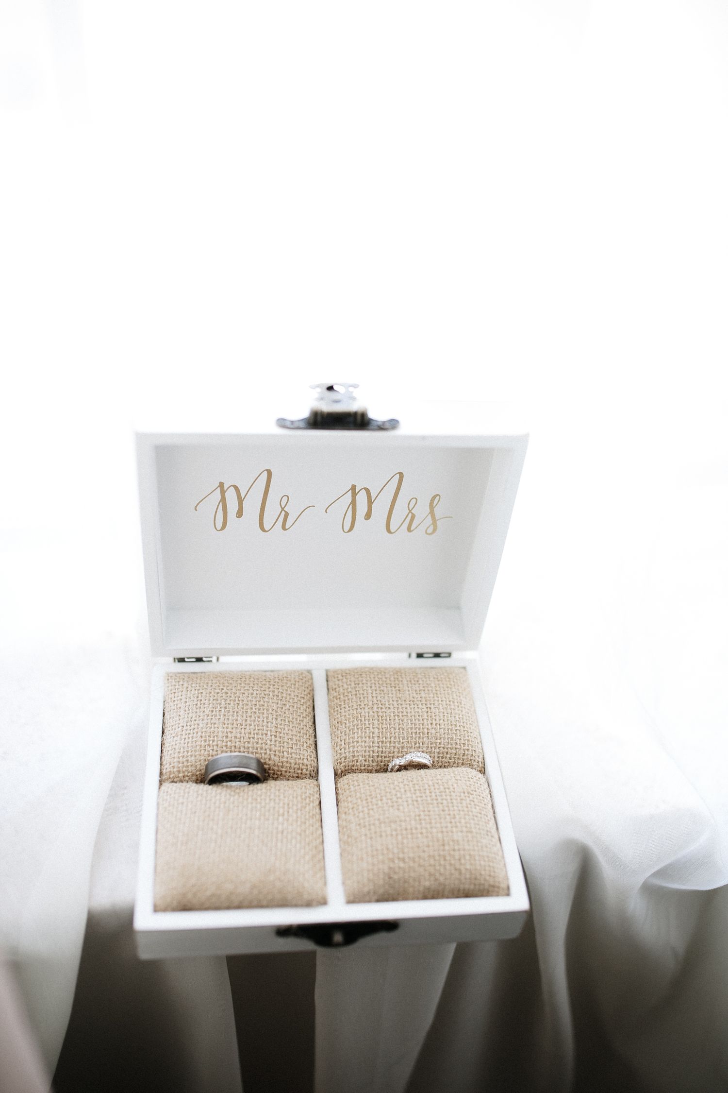 White wooden Mr. and Mrs. ring box with burlap cushions displaying wedding bands on bright white background.