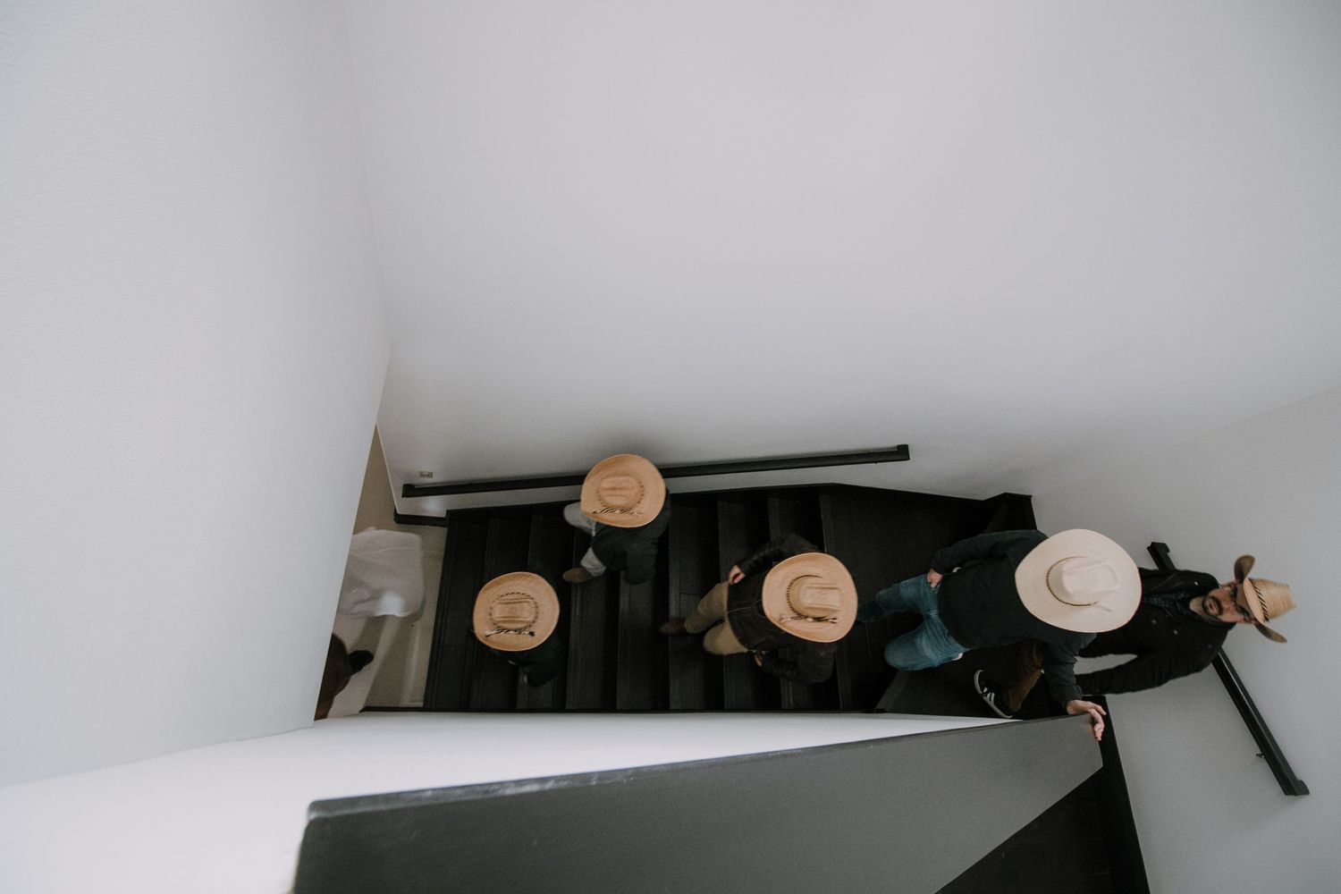 Aerial view of groomsmen wearing straw hats descending staircase before wedding ceremony.