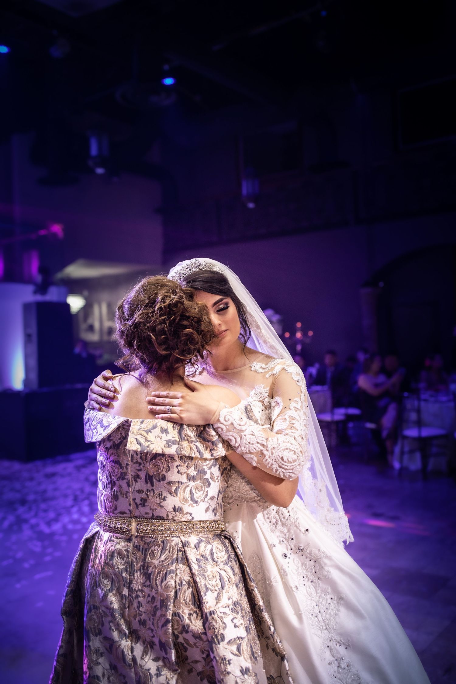 Bride and mother share an emotional first dance embrace at elegant wedding reception with purple lighting.
