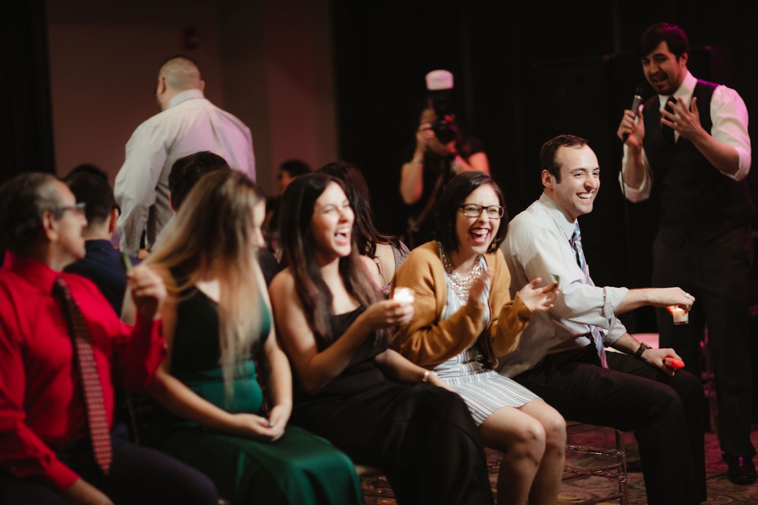 Wedding guests laughing and clapping during lively reception entertainment.