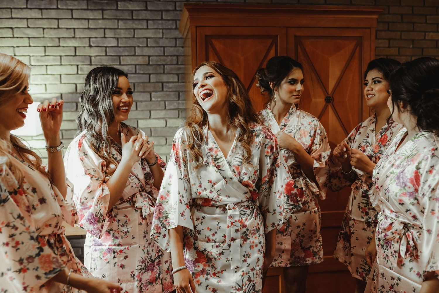 Bridesmaids laughing and celebrating together in matching floral robes before the wedding.