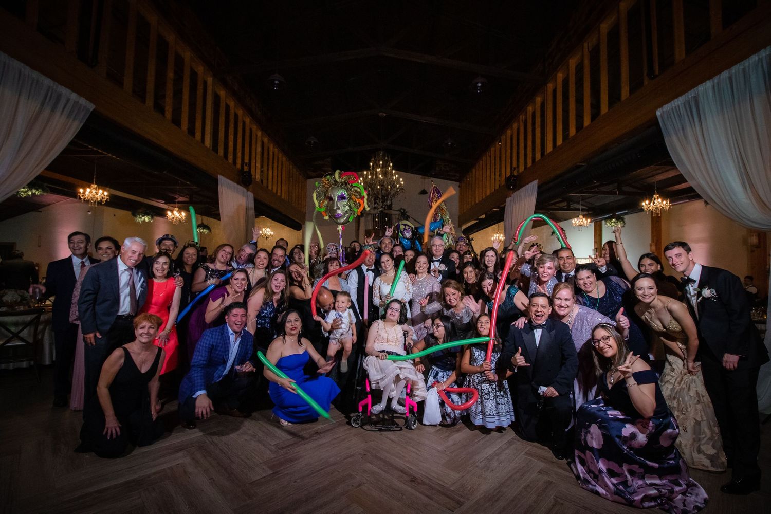 Large wedding reception group photo with guests holding colorful props in an elegant venue.