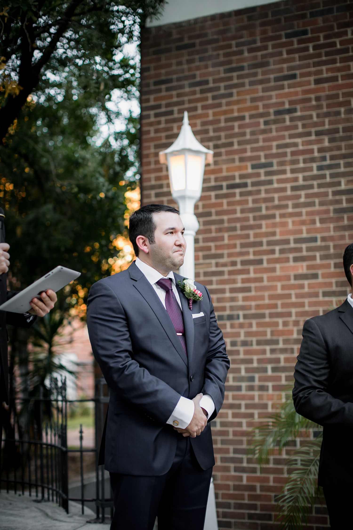 Groom in gray suit with burgundy tie watching bride walk down the aisle.