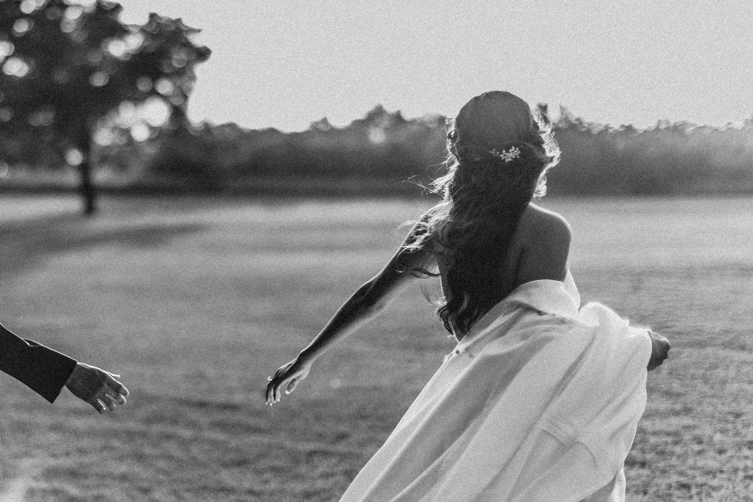A bride in a flowing white dress spins playfully in a field during an outdoor photo session.