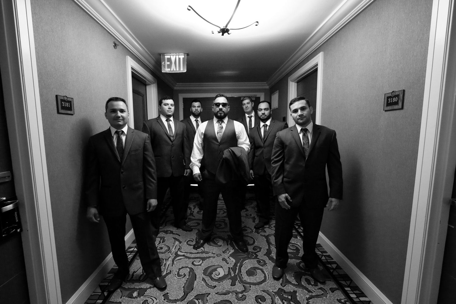 Groom and groomsmen pose in black and white photo in elegant hotel hallway for wedding party portrait.