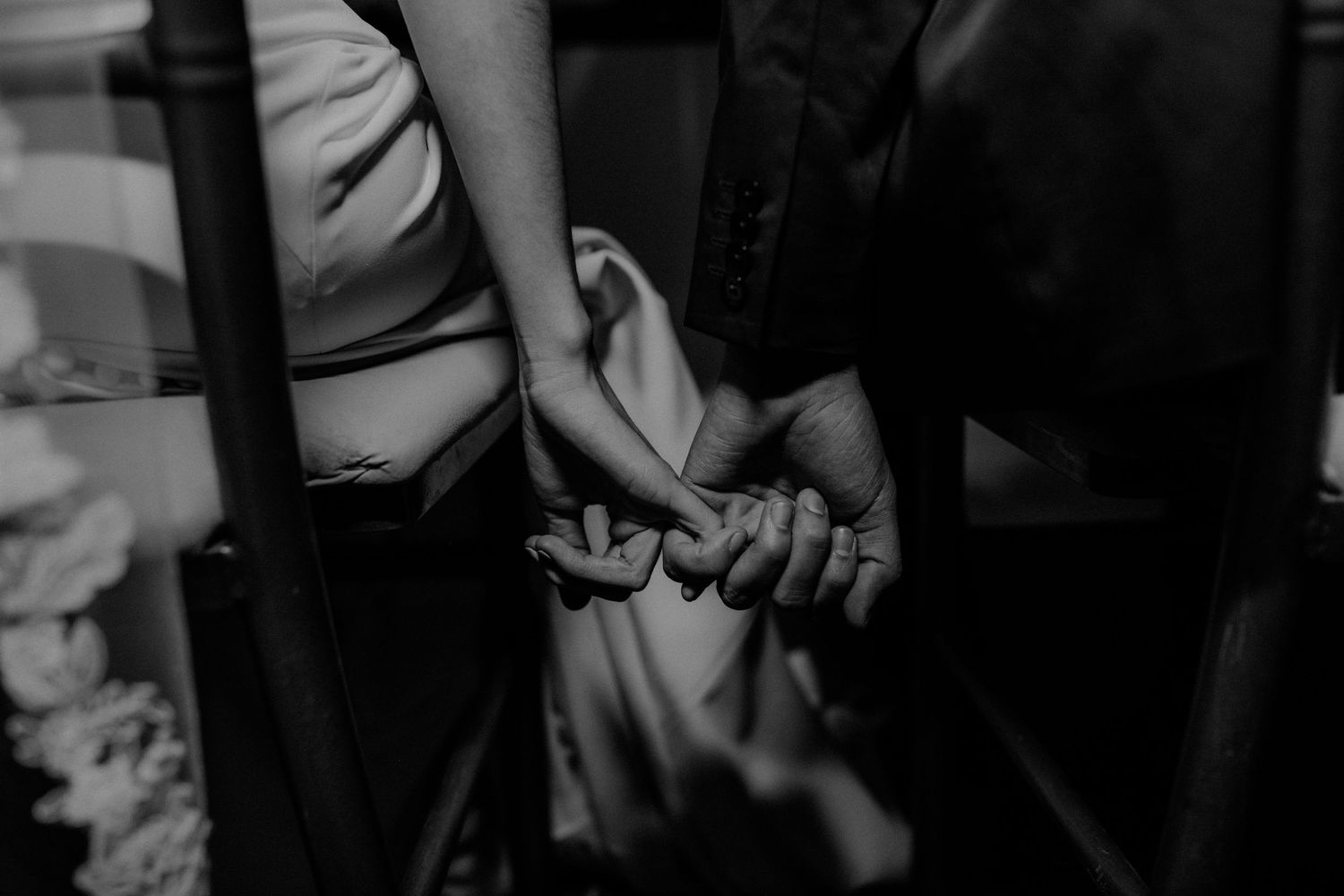 Black and white close-up of bride and groom tenderly holding hands during wedding ceremony.