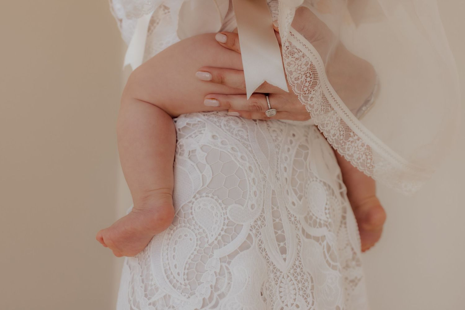 Close-up detail of tiny feet against white lace wedding dress fabric.